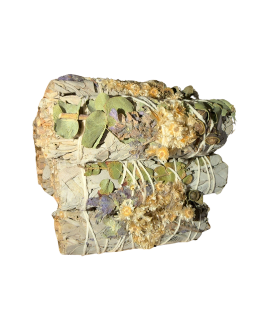 A bundle of dried white sage topped with eucalyptus, lavander, and dried botanicals wrapped in white string, photographed against a solid white background.